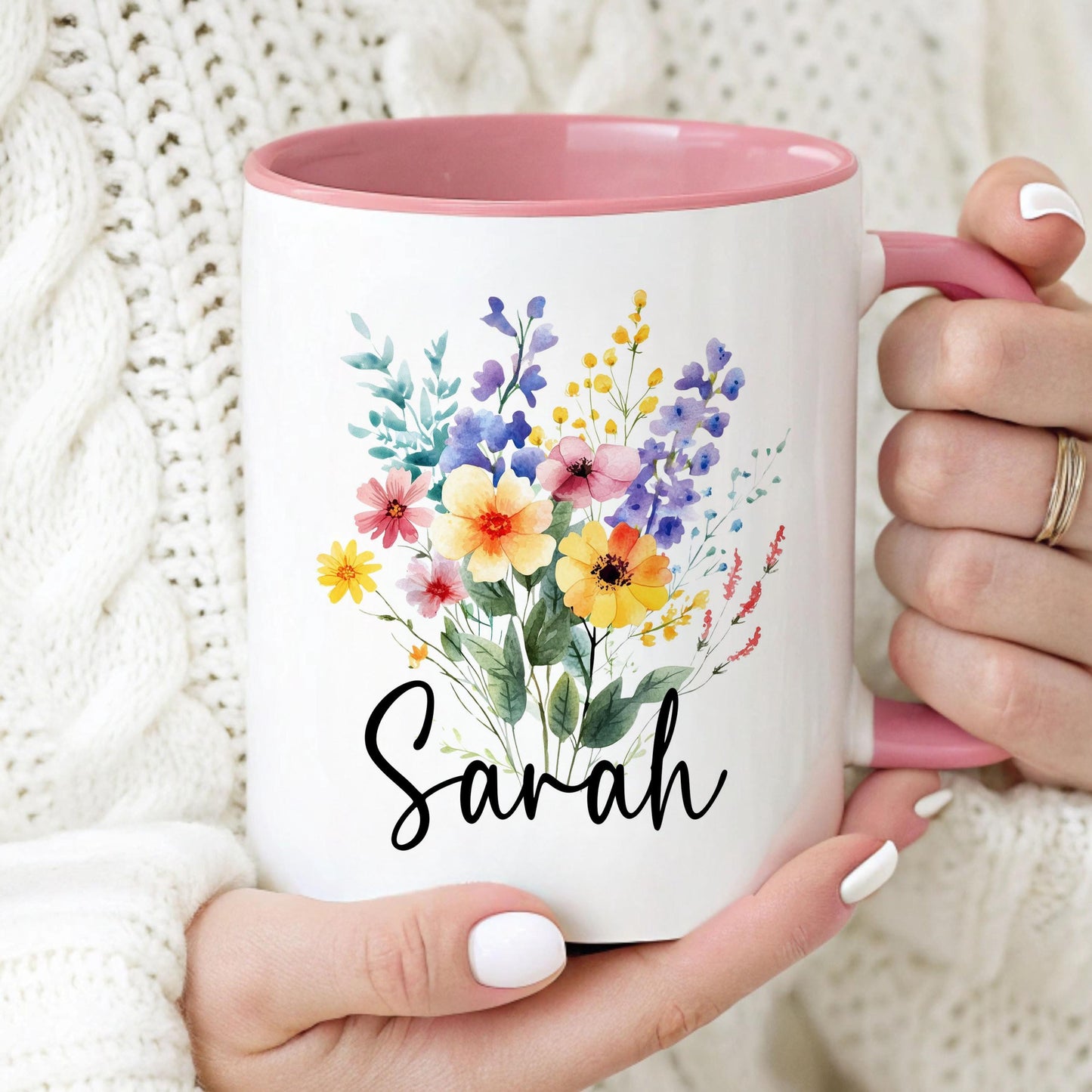 May include: A white ceramic mug with a pink rim and handle. The mug features a watercolor illustration of a bouquet of colorful flowers and the name 'Sarah' in black script.