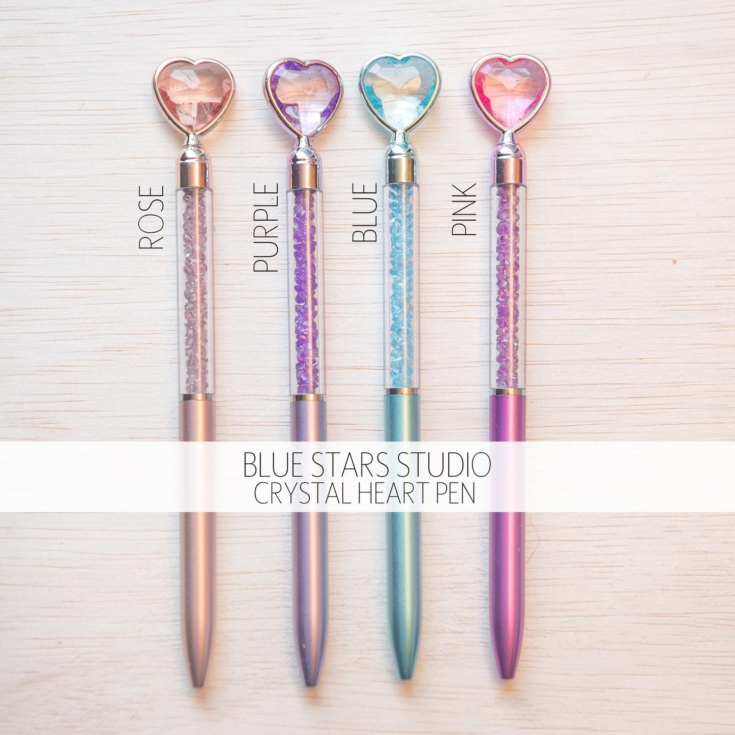 four colorful heart-shaped pens with glittery hearts attached, arranged in a row on a white background.